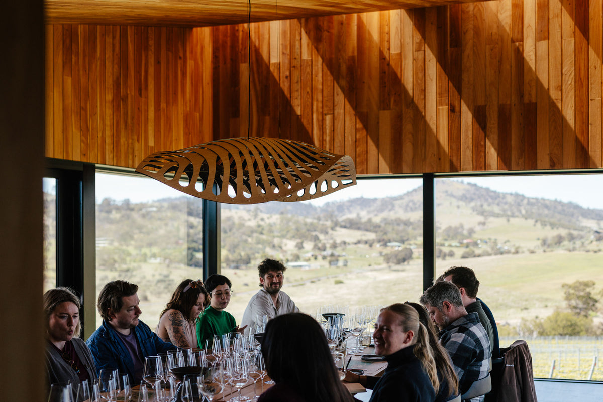 Group of people dining together in a modern wine tasting room with large windows overlooking a scenic landscape.