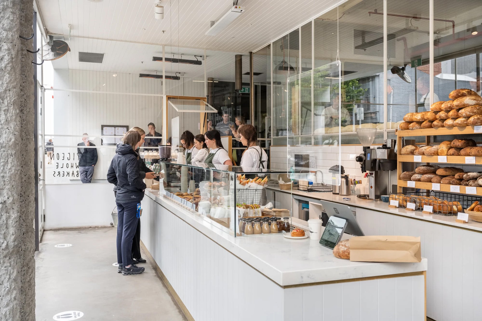 People standing in a bakery with lots of fresh bread and sandwiches